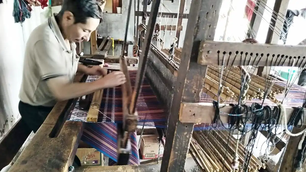 Tessuti etnici e abbigliamento estivo: tessitore guatemalteco mentre tesse su telaio manuale