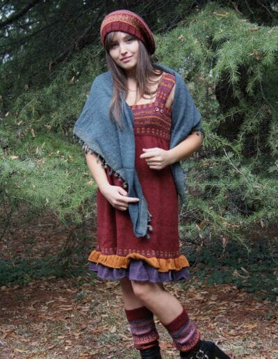 Una donna posa con un vestito in maglia rosso smanicato sotto ad un grande abete