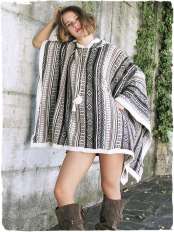 Donna davanti a un muro chiaro con edera, indossa un poncho rettangolare in lana di alpaca, etnico toni naturali, con cappuccio, modello Mexico.