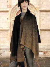 Donna dai capelli neri con mantella in baby alpaca nero e marrone, fantasia puntinata, davanti a un portale in pietra decorata, modello Pampa.