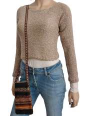 Su sfondo bianco, donna con maglioncino corto beige in baby alpaca e cotone Pima, modello Fiona, jeans e portacellulare etnico peruviano.